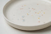 Détail d'une assiette en céramique blanche avec confettis de couleur.