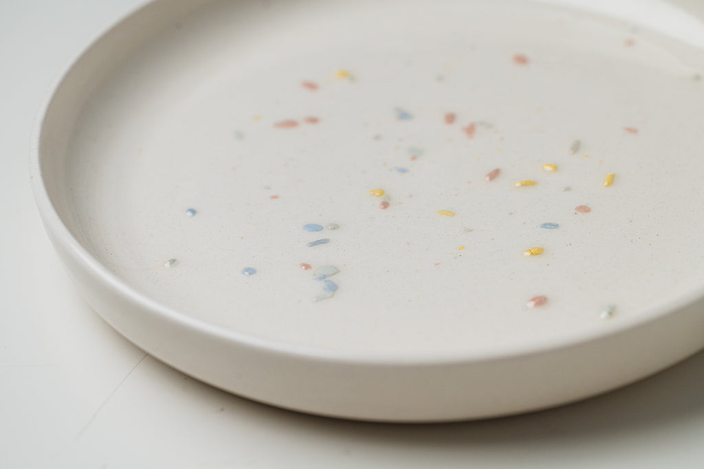 Détail d'une assiette en céramique blanche avec confettis de couleur.